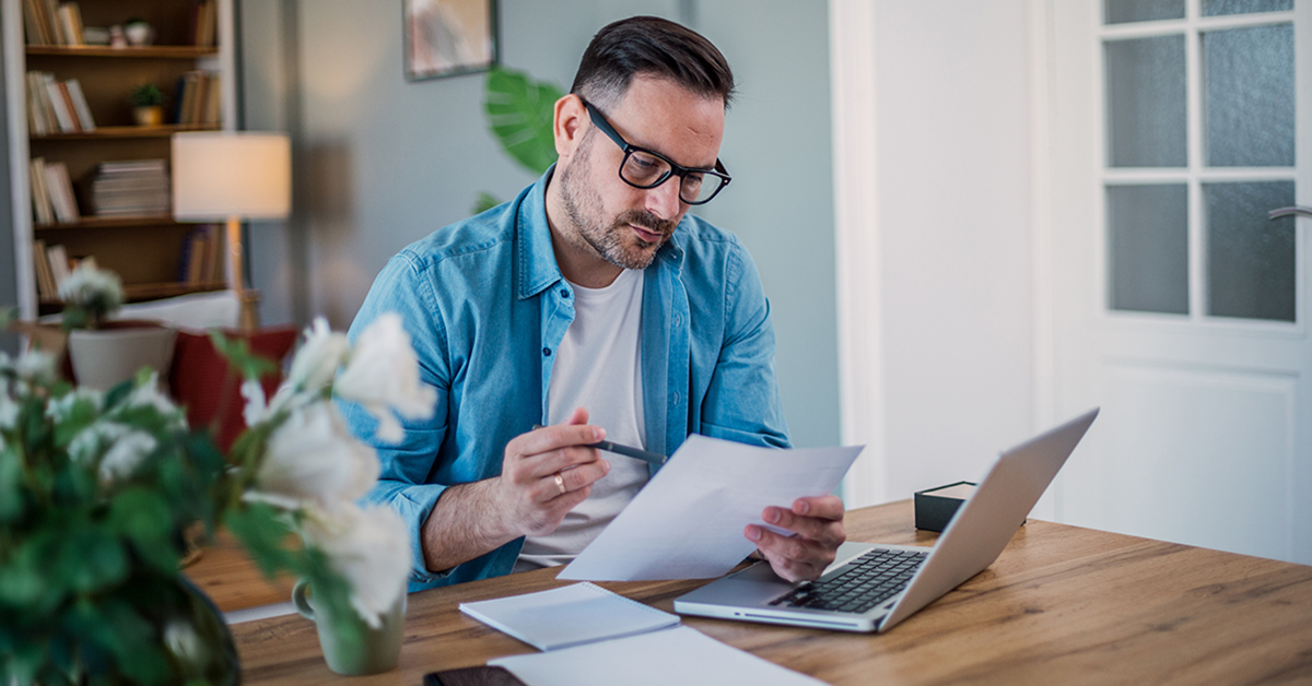 Man looks at laptop and paperwork