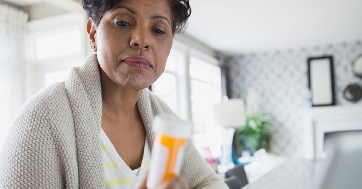 Woman sitting at home reading a prescription bottle