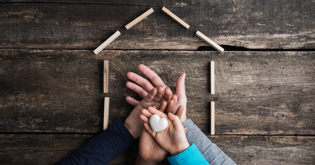Outline of a house with four hands on top of each other holding a white, heart-shaped rock
