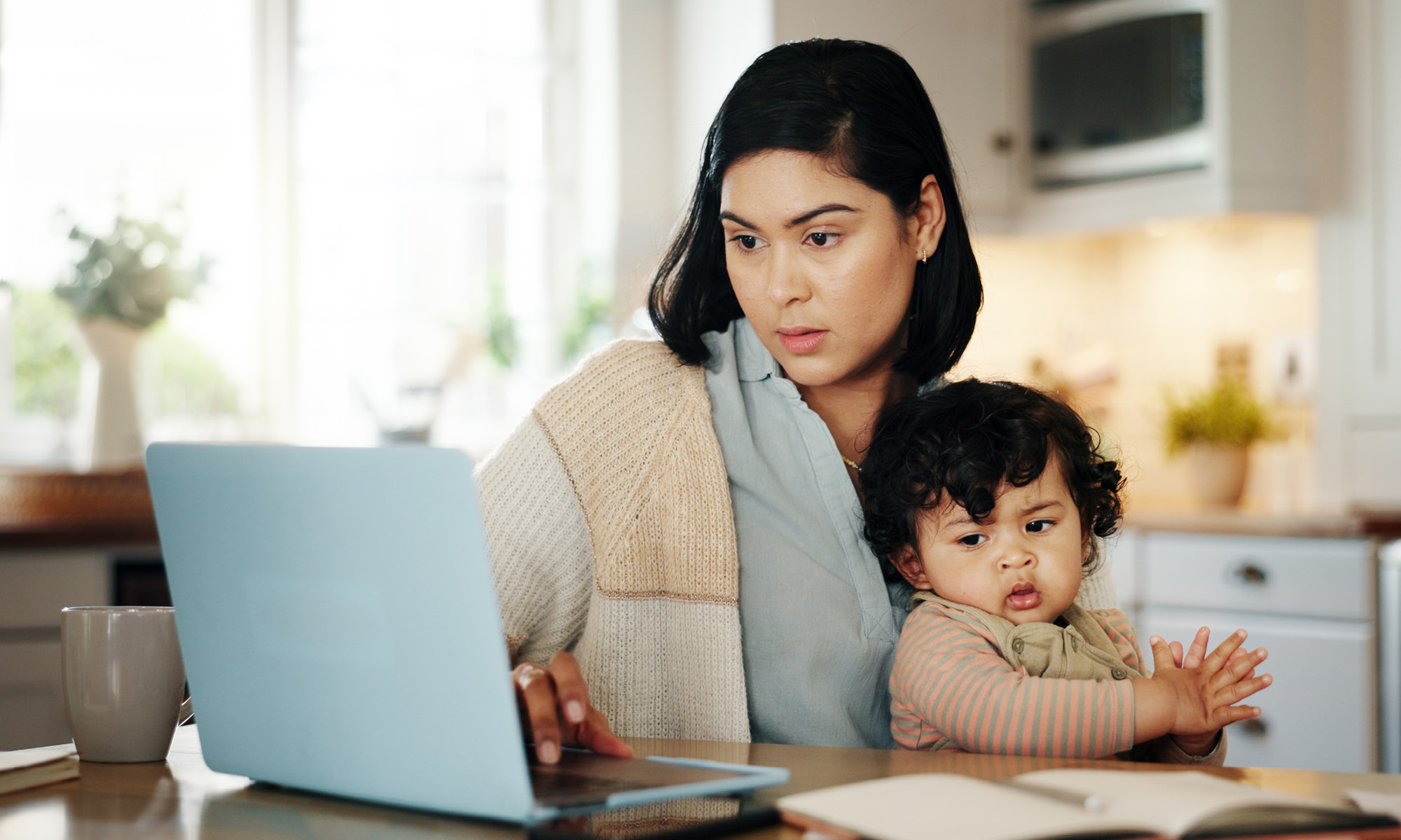 Mother holding baby on her lap while looking at her laptop