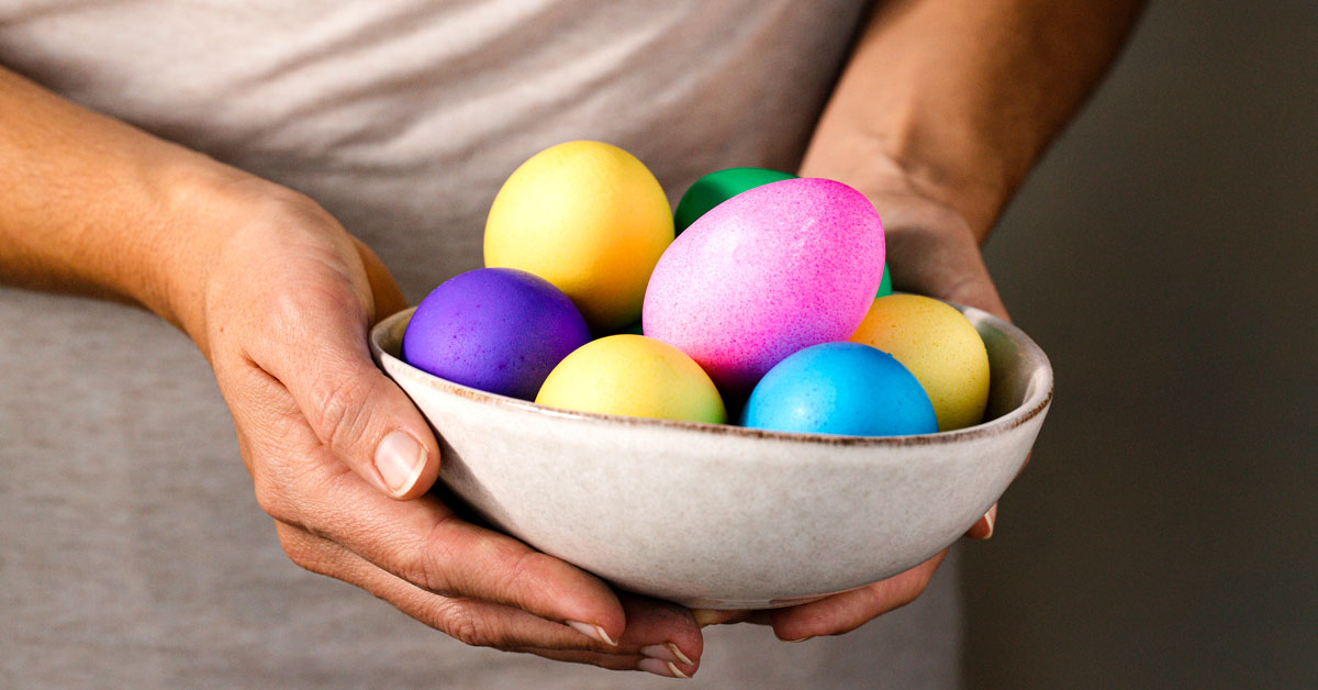 Hands holding a bowl of colored eggs.