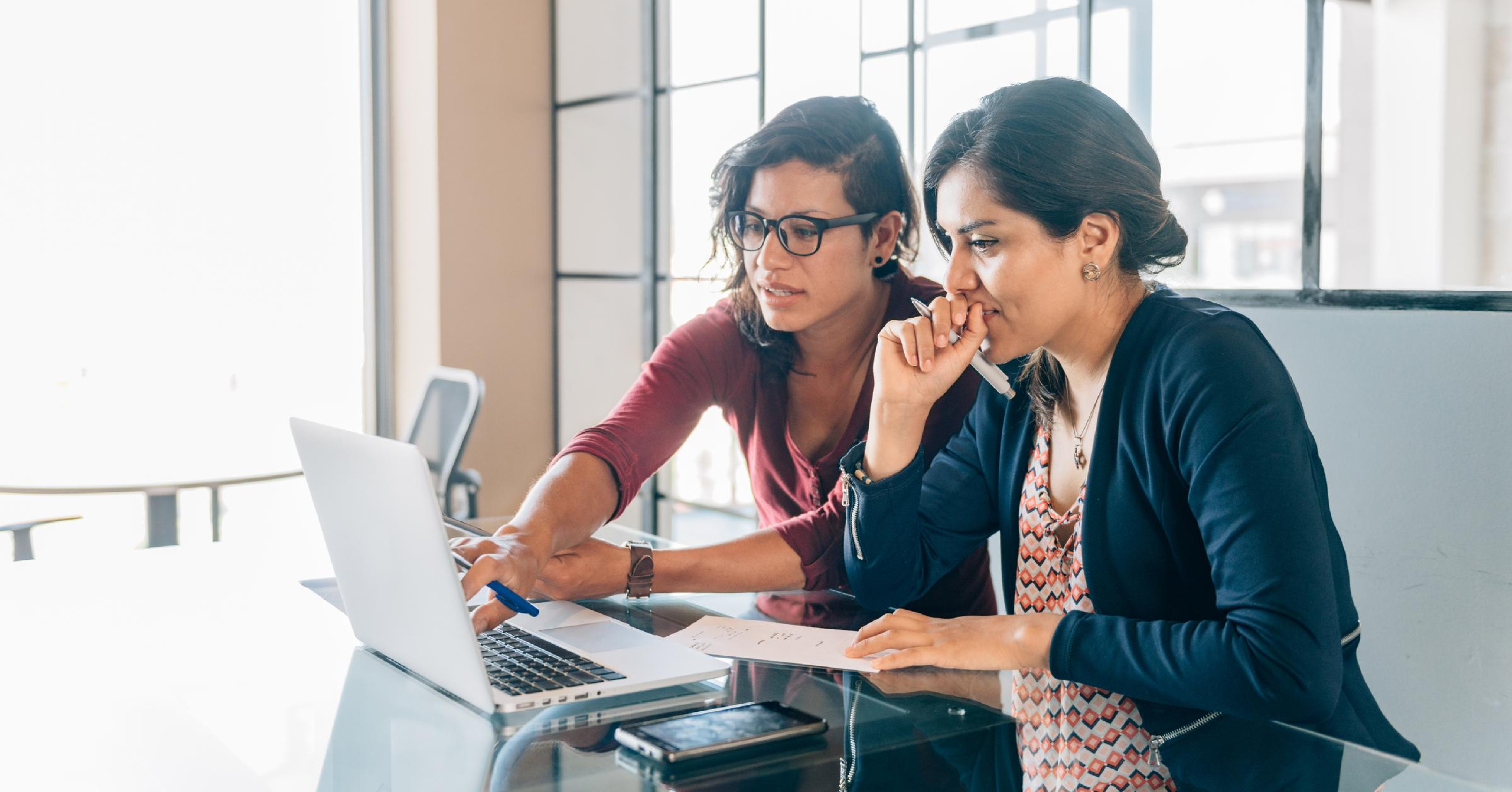 Two business women sitting at a table and looking at a laptop computer